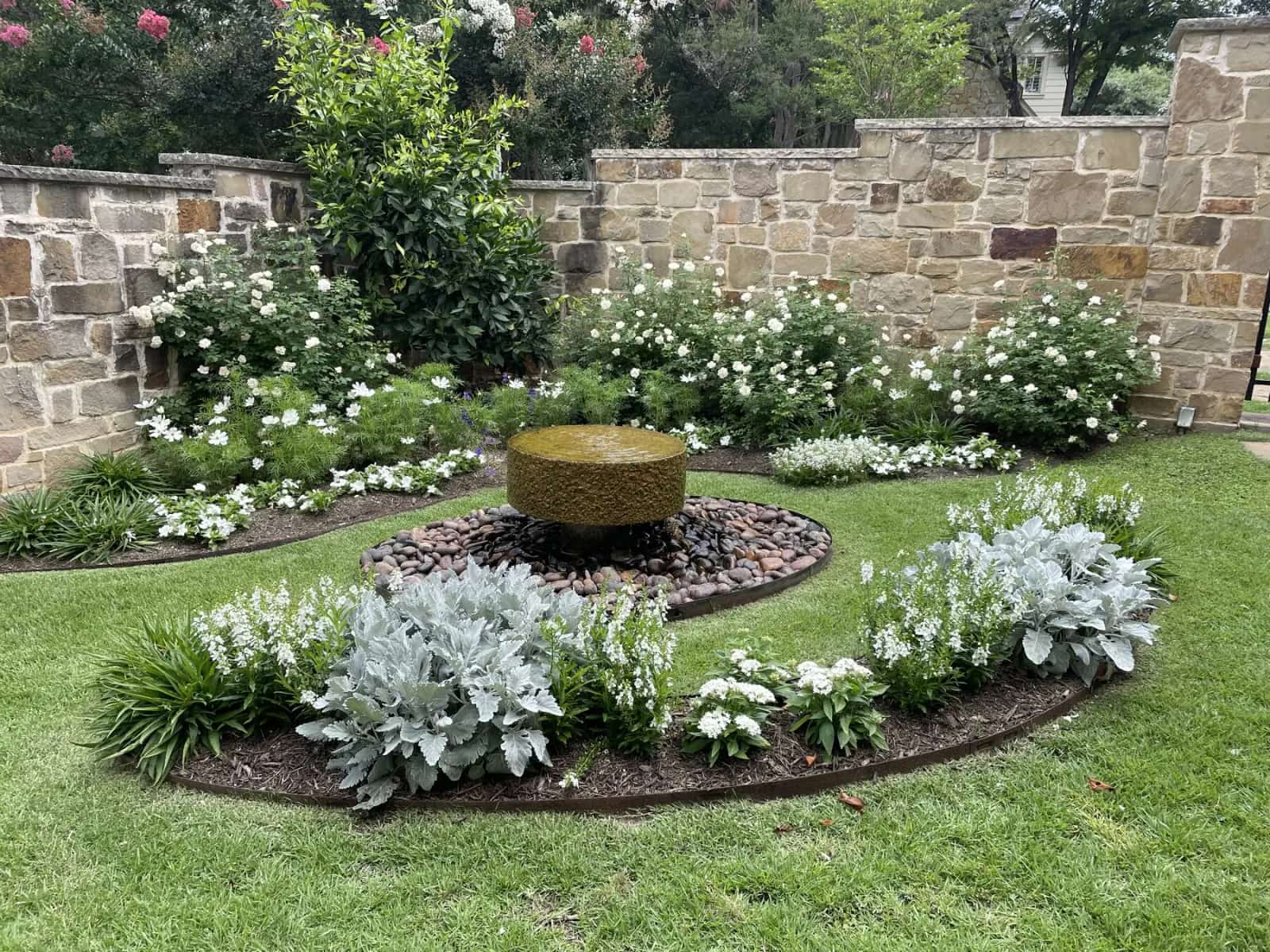 Layered Austin garden with stone wall, lawn, and flowering plants